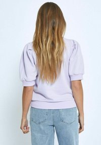 Lila tröja med puffärmar, ribbade manschetter och fåll, parat med ljusblå denimjeans med bakfickor och sömdekoration.