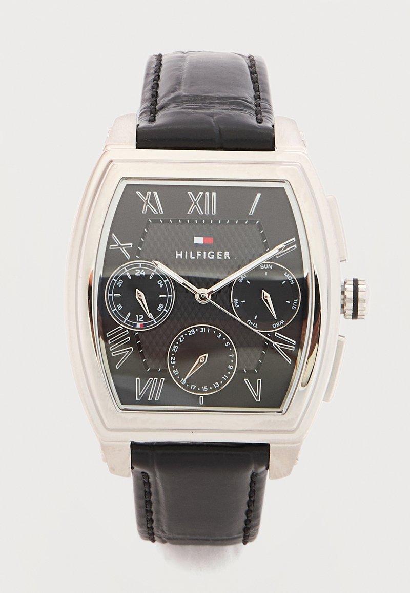 Τετράγωνο ασημένιο ρολόι με μαύρο καντράν, ρωμαϊκούς αριθμούς, τρεις υποκαντράν, μαύρο δερμάτινο λουράκι και λογότυπο Hilfiger στο κέντρο.
