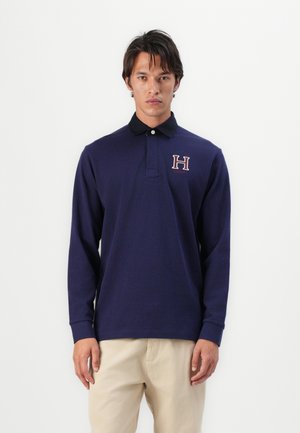 Polo à manches longues en marine avec un col noir, arborant un logo "H" brodé sur la poitrine. Fabriqué en coton doux.