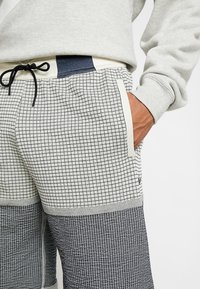 Grå och svart rutiga joggingbyxor med sidofickor, elastisk midja och kontrasterande marinblå detaljer, med en texturerad tygdesign.