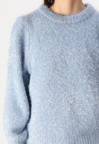Light blue sweater with a fuzzy texture, ribbed round neckline, and slight puff sleeves, featuring subtle silver accents.