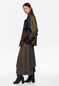 Večplasten kariran krilo v rjavi barvi z modrimi in oranžnimi akcenti; prevelik večbarven plašč temno zelene in mornarsko modre barve; črne škornje s blokastim petkom.