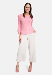 Maglione rosa chiaro, lavorato a maglia, con scollatura tonda e maniche a tre quarti, abbinato a pantaloni bianchi larghi e sandali rosa con strap.