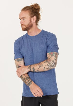 Blå, kortærmet T-shirt med et struktureret mønster, der har rund hals og broderet logo på brystet. Bæres med sorte shorts.