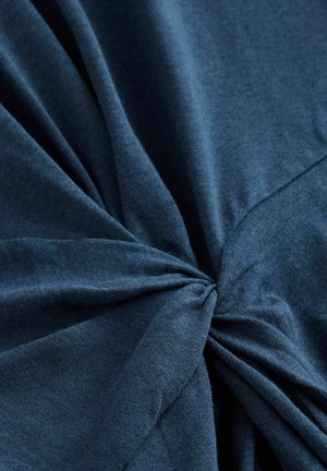 Dunkelblauer Baumwollstoff mit weicher Textur, der ein verdrehtes Knotendetail in der Mitte und sanfte Falten zeigt, die nach außen strahlen.