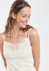 Top bianco senza maniche con spalline regolabili e dettaglio in pizzo sul collo. Tessuto morbido a coste con una vestibilità comoda.