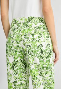 Groene en witte gestreepte broek met een gedetailleerd bloemmotief, contrasterende stiksels en een metalen sluiting op de tailleband.