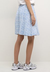 Jupe bleue avec un motif floral blanc, arrivée au genou, fabriquée en tissu léger. Assortie à des chaussures de sport blanches et grises.