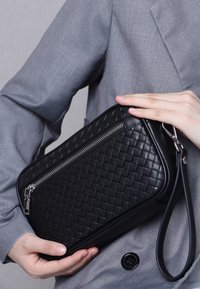 Black woven leather clutch bag with a silver zipper, detachable wrist strap, and sleek, rectangular shape. Textured with a quilted pattern.