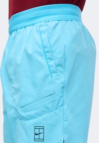 Gros plan sur un short de sport bleu clair avec deux poches latérales et un petit logo Nike noir près de l'ourlet sur la jambe gauche.