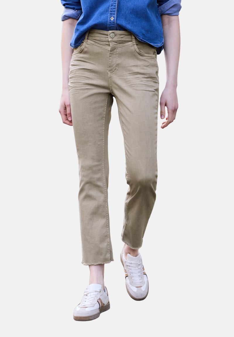 Personne portant un pantalon beige court, des baskets blanches et une chemise bleue à manches longues avec les manches retroussées marchant vers l'avant.
