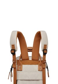 Backpack with beige fabric, brown leather accents, padded straps, and adjustable buckles. Features a front zipper pocket and reinforced stitching.