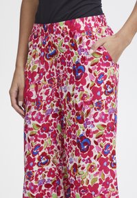 Pantalons larges floraux avec un fond rose vif, ornés de fleurs bleues, rouges et vertes. Taille élastique et poches latérales.