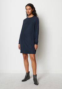 Navyblaues, langärmliges Kleid mit geradem Schnitt, weicher Textur und Rundhalsausschnitt. Kombiniert mit schwarzen Knöchelstiefeln. Einfaches und modernes Design.