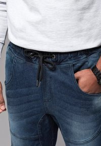 Pantaloni jogger blu scuro in denim, con vita elasticizzata e cordino, tasche laterali e una finitura testurizzata.