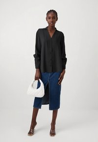 Blusa preta com botões e mangas compridas, combinada com uma saia midi de ganga com uma fenda frontal, e uma mala branca acolchoada.