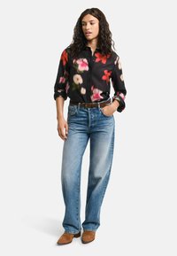 Camicia a fiori nera con bottoni e maniche arrotolate, abbinata a jeans a gamba larga azzurri e stivali con tacco marroni. Accentazioni con una cintura semplice.
