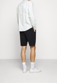 Ljust grå linne skjorta med långa ärmar, marinblå shorts, vita sneakers och vita strumpor. Klädseln har en avslappnad passform och uppvikt fåll på shorts.
