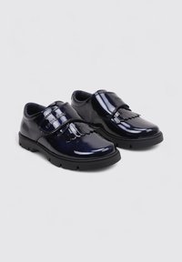 Chaussures en cuir verni bleu marine avec une sangle en velcro, des détails décoratifs en frange, une semelle extérieure en caoutchouc noir et un bout arrondi.