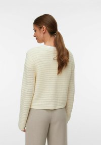 Maglione a maglia crema con motivo a righe orizzontali, collo rotondo e maniche lunghe, abbinato a pantaloni beige chiaro.