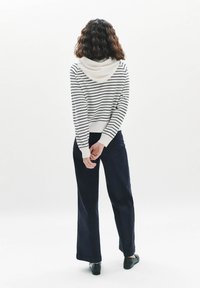 Felpa a righe bianche e blu navy con tasca frontale, abbinata a pantaloni palazzo blu navy e scarpe nere, vista da dietro. Texture liscia.