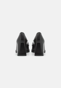 Černé kožené lodičky na vysokém podpatku se čtvercovým blokovým podpatkem, hladkým povrchem a jednoduchým designem, s výrazným prošíváním podél okrajů.