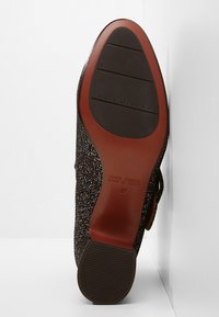 Suela de zapato negra texturizada con un acento rojo y un patrón estriado. Presenta un logo de marca y una impresión de tamaño cerca del talón.