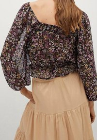 Kwiatowa, przezroczysta bluzka z bufiastymi rękawami, z marszczonym dekoltem w czarnym, purpurowym i żółtym wzorze, zestawiona z beżową spódnicą plisowaną.