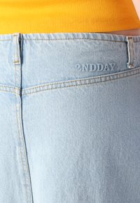 Jean en denim bleu clair avec une texture lisse, arborant un logo subtil en relief "2NDDAY" près de la taille et des coutures contrastées.