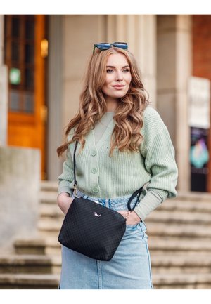 Black quilted handbag with a pink logo, paired with a light green knitted cardigan and denim skirt, featuring buttons and rolled sleeves.