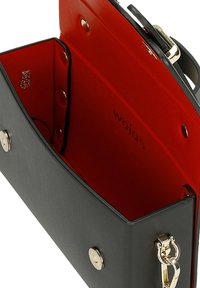 Borsa a tracolla in pelle nera con fodera interna rossa, chiusura magnetica argento, e una clip dorata removibile sul lato.