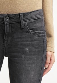 Jeans de mezclilla negra con un corte slim, que cuentan con un cierre de botón clásico, desgastes sutiles y costuras en contraste.