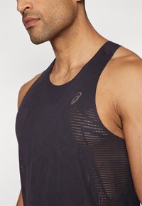 Débardeur de sport bleu marine foncé avec une texture en maille respirante, un motif géométrique subtil et un logo sur le côté supérieur gauche.