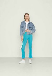 Jaqueta de ganga azul-claro, t-shirt cropped branca e calças turquesa à boca de sino. Modelo usa ténis brancos e carrega uma pequena bolsa branca.