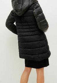 Czarna kurtka puchowa z kapturem, z pikowaną fakturą, długimi rękawami i lekko rozkloszowanym dołem. Gładki, błyszczący materiał, średniej długości fason.