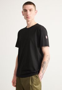Black cotton t-shirt with a crew neck, short sleeves, and a small circular logo on the left sleeve. Smooth texture, relaxed fit.