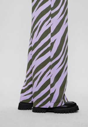 Hlače širokega kroja v barvi lavande in olivno zeleni zebri, izdelane iz teksturirane tkanine, v kombinaciji z debelimi črnimi platformnimi čevlji.