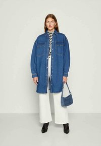 Dolga modra denim srajca z dvema žepoma na prsih, oversize kroj, v kombinaciji z belimi širokimi hlačami in majhno modro torbico. Črne gležnjarje na peto.