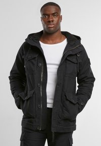 Sort hættejakke lavet af holdbart materiale, med flere forreste lommer, lynlås lukning og fleece-foring indeni for varme.