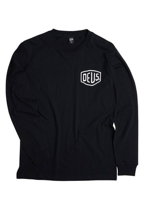 Black long-sleeve t-shirt made from cotton. Features white shield logo with "DEUS" text on the left chest. Crew neck and standard fit.