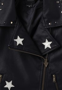 Zwart leren jack met zilveren sterapplicaties op de kraag en borst, zilveren rits en drukknoopsluiting, en een zichtbaar "Made in China" maat 8 label.