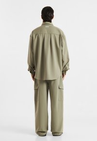 Khaki oversized skjorte med krave, skuldersømme og lange ærmer, parret med matchende cargo bukser med sidelommer.