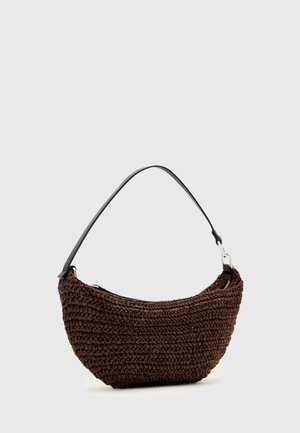 Sac à main tissé marron avec une forme courbée et une bandoulière unique noire sur fond gris clair uni.