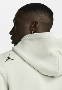 Sweat à capuche vert clair en tissu doux, avec une capuche à bord blanc et un logo Jordan noir au dos.