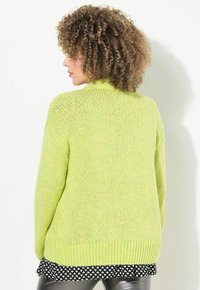 Pull en tricot vert avec une coupe ample, featuring un ourlet côtelé. La texture est douce et épaisse, offrant un look confortable.