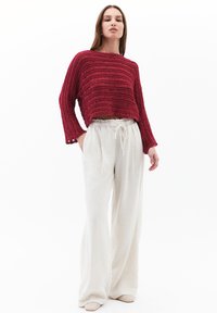 Pull court bordeaux avec un motif texturé et côtelé et des manches larges, associé à un pantalon en lin beige clair avec une taille élastique.