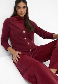 Burgunderfarbener Cardigan mit V-Ausschnitt, Knopfleiste und geripptem Textur, kombiniert mit einem burgunderfarbenen Rollkragenpullover und passenden samtigen Cordhosen.