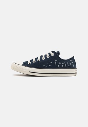 Zapatillas de lona azul marino con patrones de estrellas blancas, punta de goma y cordones blancos. Presenta un diseño clásico de corte bajo y una franja negra en la suela.