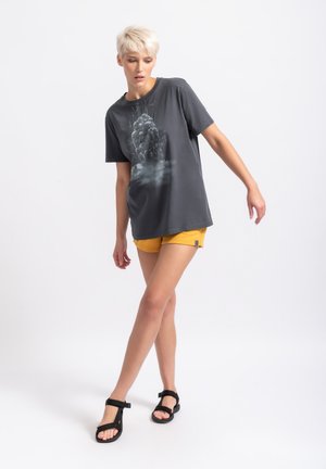 T-shirt grigia a maniche corte con un design grafico che presenta un gruppo di bolle. Abbinata a pantaloni corti gialli e sandali neri.
