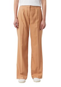 Spodnie o szerokich nogawkach wykonane z jasnoróżowego materiału, z przodu z plisami, o gładkiej fakturze i dopasowanym kroju. Noszone z białymi tenisówkami.